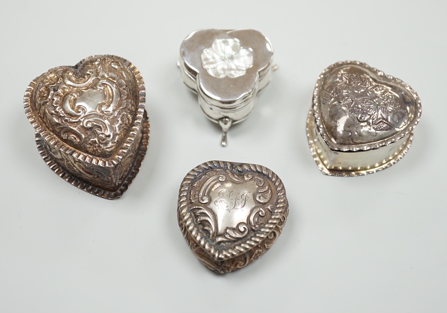 Three Victorian/Edwardian repousse silver heart shaped trinket boxes, largest 56mm and a similar mother of pearl inlaid 'pansy' trinket box, by Saunders & Shepherd, gross weight 1106 grams.